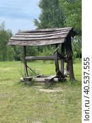 Antique wooden water well. Old wooden well.Old wooden wheel and bucket of water inside on grass ground, primitive knowhow stock photo. Редакционное фото, фотограф Екатерина Казначеева / Фотобанк Лори