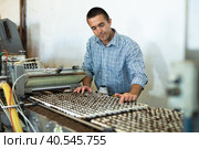 Farmer man working with automatic filling and seeding line for growing containerized seedlings of decorative plants in greenhouse. Стоковое фото, фотограф Яков Филимонов / Фотобанк Лори