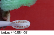 A man presses the power button on a portable portable fan. Shows operating modes. The fan blows on the brush, demonstrating the strength of the air flow. The brush falls. On a coral background. Стоковое видео, видеограф Vadzim Yakubovich / Фотобанк Лори