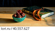 Turquoise piala with traditional oriental pattern with dates and green and gilded book of Quran on table during sunset First meal, Muslim fast Eid al, Стоковое фото, фотограф Ирина Кононова / Фотобанк Лори