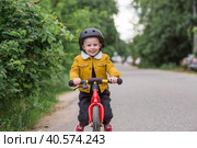 A cheerful little boy rides a running bike in a helmet outdoors. A happy child is engaged in an active sport. Protection. Life insurance and child safety. Стоковое фото, фотограф Photojuli / Фотобанк Лори