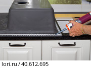 Applying black sanitary sealant with a nail gun to the edge of the kitchen sink. Installing a sink on a kitchen countertop. Стоковое фото, фотограф Коханова Наталья / Фотобанк Лори