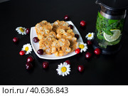 Домашний десерт для детей из ириски, сливочного масла и кукурузных палочек на белой тарелке, украшенной ромашками с божьими коровками и вишней рядом с чайником, в котором завариваются листья смородины, мята и лимон. Стоковое фото, фотограф Елена Яворская / Фотобанк Лори