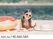 Happy cute smiling little girl in sunglasses lying on the sand on a beach in a swimsuit near a straw hat. Стоковое фото, фотограф Ирина Михайличенко / Фотобанк Лори