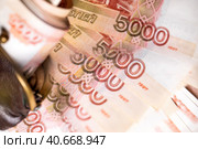 Пачка рублевых пятитысячных купюр лежит в старом кошельке на фоне денежных купюр, в расфокусе. Стоковое фото, фотограф Николай Винокуров / Фотобанк Лори