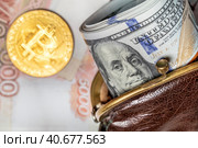 Толстая пачка сто-долларовых купюр США лежит в старом, потертом кошельке на фоне пятитысачных купюр российского рубля и монеты криптовалюты Биткоин. Стоковое фото, фотограф Николай Винокуров / Фотобанк Лори