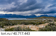 A rocky island with stunted sparse vegetation. The Beagle Canal is visible in the distance. A picturesque mountain range Martial against a cloudy sky. Argentina. Tierra del Fuego Archipelago. (2023 год). Стоковое фото, фотограф Вера Ивановна Кубарева / Фотобанк Лори