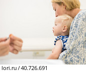 Child beeing vaccinated by pediatrician in presence of his mother. Preventive vaccination against Diphtheria, whooping cough, tetanus, hepatitis, haemophilus influenzae, pneumococcus, poliomyelitis. Стоковое фото, фотограф Matej Kastelic / Фотобанк Лори