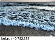 Waves with foam. Beautiful sunset. Foamy waves roll over the sandy shore. Vityazevo, Anapa, Black Sea. Tourist mecca, health resort. Colorful clouds in the evening sky. The rays reflect off the water. Стоковое фото, фотограф Юлия Петровская / Фотобанк Лори