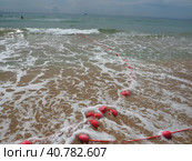 Buoys on a rope in sea water. The lifebuoys are pink restraints to alert people to the depth of the water. Rescue of the drowning. Delimiting a place on sandy beach between hotels. Wave with bubbles. Стоковое фото, фотограф Юлия Петровская / Фотобанк Лори