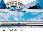 Saransk, Mordovia, Russia, 4.06.2023. The blue facade of the building with the inscription Russian Post and a double-headed Russian eagle, against the background of the reflection of clouds on the glass surface. Редакционное фото, фотограф Оксана Медведева / Фотобанк Лори