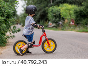 A cheerful little boy rides a running bike in a helmet outdoors. A happy child is engaged in an active sport. Protection. Life insurance and child safety. Стоковое фото, фотограф Photojuli / Фотобанк Лори