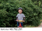 A cheerful little boy rides a running bike in a helmet outdoors. A happy child is engaged in an active sport. Protection. Life insurance and child safety. Стоковое фото, фотограф Photojuli / Фотобанк Лори