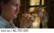 Adult girl bowed her head in thanksgiving prayer to God in church. Young woman folded hands in prayer to Christ the Redeemer. Стоковое фото, фотограф Ольга Сухарева / Фотобанк Лори