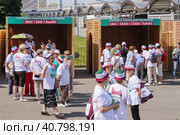 Пенсионеры в футболках и головных уборах с символикой Москвы готовятся к занятиям гимнастикой на открытом воздухе на празднике по программе «Московское долголетие» (2023 год). Редакционное фото, фотограф Сергей Никифоров-Гордеев / Фотобанк Лори