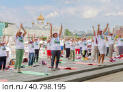 Московские пенсионеры в фирменных московских футболках и головных уборах делают гимнастику в парке Музеон на фоне храма Христа Спасителя, голубого неба и красивых облаков (2023 год). Редакционное фото, фотограф Сергей Никифоров-Гордеев / Фотобанк Лори