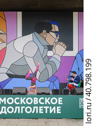 На сцене парка Музеон спортивная женщина пенсионерка демонстрирует стойку на голове. Родион Газманов комментирует происходящее в микрофон и морально поддерживает женщину. (2023 год). Редакционное фото, фотограф Сергей Никифоров-Гордеев / Фотобанк Лори