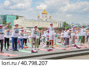 Мужчины и женщины пенсионного возраста в фирменных московских футболках и головных уборах в московском парке Музеон выполнят гимнастику, стоя на разноцветных гимнастических ковриках на фоне храма Христа Спасителя, голубого неба и кучевых облаков (2023 год). Редакционное фото, фотограф Сергей Никифоров-Гордеев / Фотобанк Лори