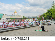 Пенсионеры, участники спортивного праздника программы "Московское долголетие", в фирменных московских футболках и шапочках, стоя на разноцветных гимнастических ковриках, выполняют гимнастику под руководством опытного тренера в парке Музеон на фоне московских храма Христа Спасителя, московсих зданий и неба с красивыми белыми облаками (2023 год). Редакционное фото, фотограф Сергей Никифоров-Гордеев / Фотобанк Лори