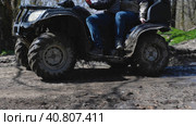 Close-up of a dirty black ATV riding on a dirt forest road. Water is flowing from it as it has just passed through a puddle. Side view. Extreme type of outdoor activities. Riding on a quad bike. Стоковое фото, фотограф Воловодов Владимир / Фотобанк Лори