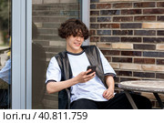 Young man reading funny message on phone while sitting at an outdoor cafeteria table. Стоковое фото, фотограф Евгений Харитонов / Фотобанк Лори