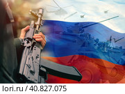A rifle in the hands of a Russian soldier against the background of the flag of the Russian Federation and the silhouettes of military armored vehicles and aviation. The concept of mobilization. Стоковое фото, фотограф Алексей Игнатов / Фотобанк Лори