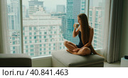 Silhouette of young woman drinking delicious coffee near window with big city outside. Relaxed girl enjoys morning cappuccino on weekend in the metropolis. Slow motion. Стоковое фото, фотограф Ольга Сухарева / Фотобанк Лори