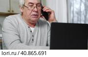 Serious senior man wearing glasses Talking mobile phone sitting at desk at home workplace with laptop. Retired male working chatting colleagues. Old worker talk on cellphone work on computer gadget. Стоковое видео, видеограф Марина Демидюк / Фотобанк Лори