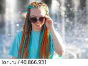 A teenager girl in a bright turquoise summer t-shirt with colored orange-turquoise African braids in her hair happily looks at camera. Child with disabilities. Equal opportunities for all. Стоковое фото, фотограф Ирина Михайличенко / Фотобанк Лори