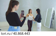 Young woman shooting a video on her phone as another woman takes measurements of the body of a slim model. Стоковое видео, видеограф Константин Шишкин / Фотобанк Лори