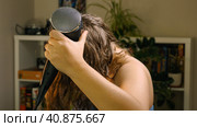 A Caucasian woman dries her hair with a hair dryer and comb while standing in the living room. Selective Focus. The concept of beauty and hair care. Стоковое фото, фотограф Воловодов Владимир / Фотобанк Лори