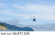 Лёгкий четырёх местный вертолёт компании "Robinson Helicopter" летит над побережьем Охотского моря с туристами на борту. Туризм на  острове Сахалин. (2023 год). Редакционное видео, видеограф Эльвира  Трощенкова / Фотобанк Лори