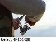 Old man fishing. Senior gray haired fisherman throws a spinning from shoreside at sunset, twisting a coil. Positive elderly male angling at lake, rotating reel rod. Retired fisher enjoying his weekend. Стоковое фото, фотограф Марина Демидюк / Фотобанк Лори
