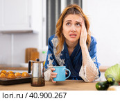 Young woman suffering from migraine, drinking coffee in home kitchen. Стоковое фото, фотограф Татьяна Яцевич / Фотобанк Лори