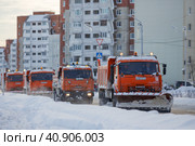 Снегоуборочные машины на улицах города. Четыре оранжевых грузовика едут по дороге на фоне панельных домов. Кругом снег и сугробы. Холодная погода. Магадан, Россия. Редакционное фото, фотограф Андрей Степанов / Фотобанк Лори