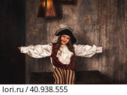 Portrait of smiling pirate sitting on chest arms to sides in hold of pirates ship, playful looking at camera. Charming child girl actress in corsair image. Theatre perform concept. Copy ad text space. Стоковое фото, фотограф Aleksandr Golubev / Фотобанк Лори