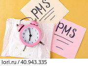 Женская гигиеническая прокладка в упаковке, будильник на желтом фоне. Приход менструации, ПМС, критические дни. Стоковое фото, фотограф Айгуль Миннибаева / Фотобанк Лори