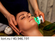 Close-up of beautician hands doing led light therapy to young woman in medical spa salon. Facial phototherapy for skin pore cleaning. Anti-aging treatments and photo rejuvenation procedure. Copy space. Стоковое фото, фотограф Aleksandr Golubev / Фотобанк Лори