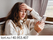 Upset girl Sitting on couch at home with cellphone. Стоковое фото, фотограф Гладских Татьяна / Фотобанк Лори