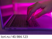 Person typing at laptop computer at night. Female uses keyboard, shakes buttons with fingers. Internet security, cyber attack. Trendy neon light. Creative vivid color of ultraviolet red and blue. Стоковое фото, фотограф Марина Демидюк / Фотобанк Лори