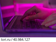 Person typing at laptop computer at night. Female uses keyboard, shakes buttons with fingers. Internet security, cyber attack. Trendy neon light. Creative vivid color of ultraviolet red and blue. Стоковое фото, фотограф Марина Демидюк / Фотобанк Лори