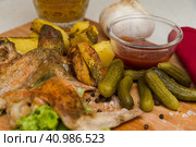 Fried chicken wings served on a wooden Board with Idaho potatoes, pickled gherkins and fresh lettuce leaves. A mug of beer is next to it. жареные куриные крылышки подаются на деревянной доске с картофелем Айдахо, маринованными корнишонами и свежими листьями салата. Рядом с ним стоит кружка пива. Стоковое фото, фотограф Дмитрий Березнев / Фотобанк Лори