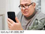 Hoary old man looking at web camera, holding phone, talking with children, wife online. Senior grandpa smiling chatting with friends, family via video call. Modern technologies and older generation. Стоковое фото, фотограф Марина Демидюк / Фотобанк Лори