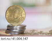 Деньги. Монета номиналом в 10 рублей на стопке монет в 1 рубль. На фоне 100-рублевых купюр. Стоковое фото, фотограф E. O. / Фотобанк Лори