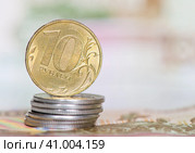 Деньги. Монета номиналом в 10 рублей на стопке монет в 1 рубль на фоне 100-рублевых банкнот. Стоковое фото, фотограф E. O. / Фотобанк Лори