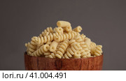 Gluten Free Cornmeal Pasta in wooden Bowl. Spiral Raw Macaroni from Blend of Corn and Rice flour rotating on Turntable. Close Up, Front View. Uncooked Rotini Pasta is Spinning. Food Background. Ad. Стоковое видео, видеограф Марина Демидюк / Фотобанк Лори