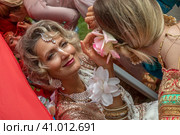 Красивая женщина помогает девушке одеть индийское сари на фестивале День Индии в Москве, Россия (2023 год). Редакционное фото, фотограф Николай Винокуров / Фотобанк Лори