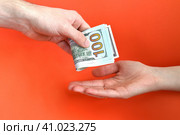 Hand giving folded money usa dollar in other hand on a red background. Bribe concept. Стоковое фото, фотограф Татьяна Терехина / Фотобанк Лори