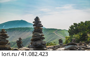 Mountains against the sky. On the slopes there is green vegetation, a winding dirt road. In the foreground there are several pyramids made of stones. Kamchatka. Стоковое фото, фотограф Вера Ивановна Кубарева / Фотобанк Лори