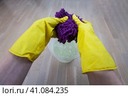 Руки в желтых хозяйственных перчатках отжимают мокрую фиолетовую половую тряпку в ведро. Стоковое фото, фотограф Константин Григорьев / Фотобанк Лори
